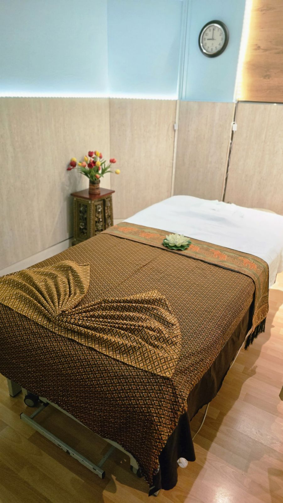 Behandlungsraum mit Massageliege, Blumen und Wanduhr